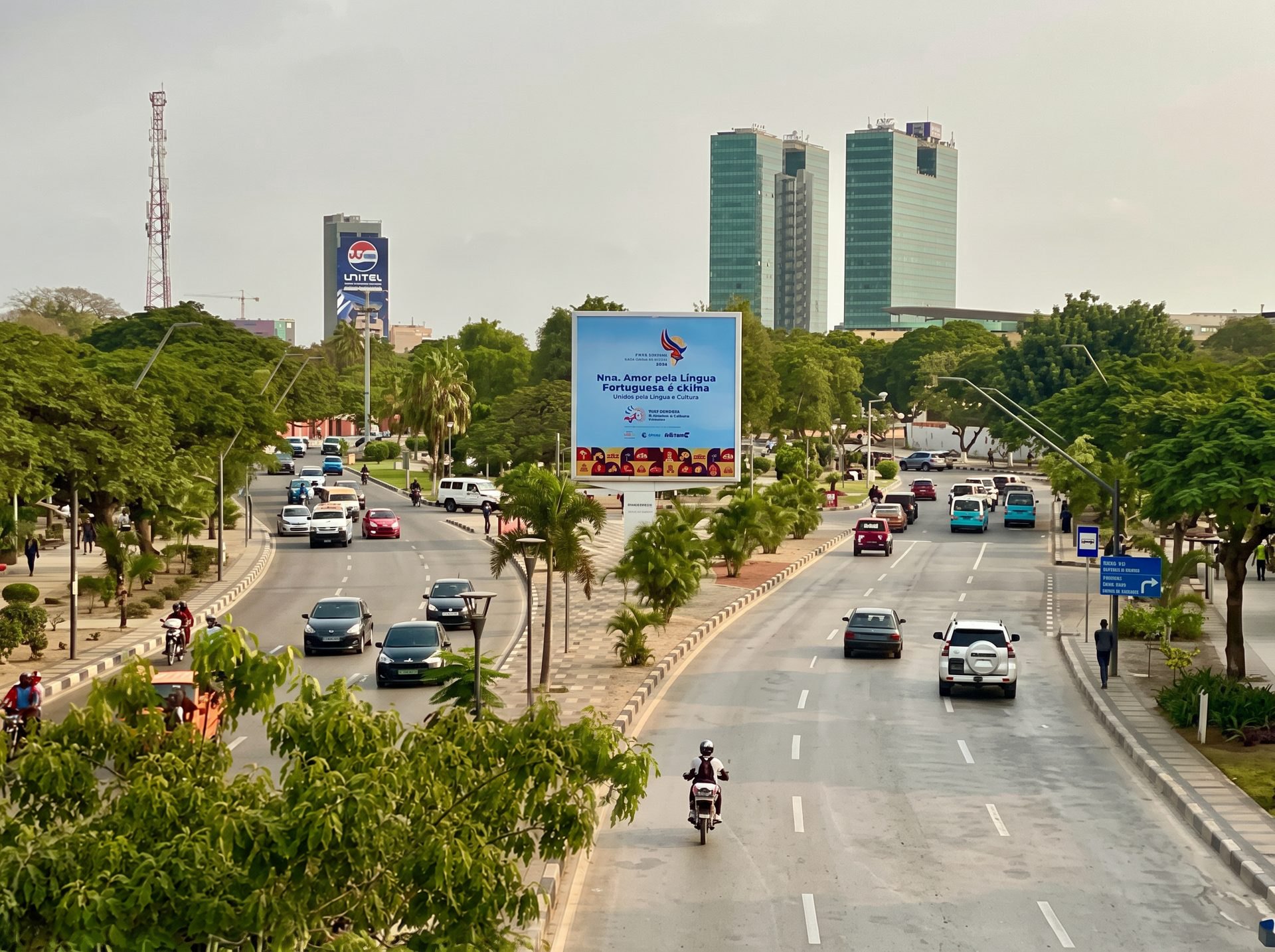 A tree-lined avenue in central Luanda with traffic and office towers
